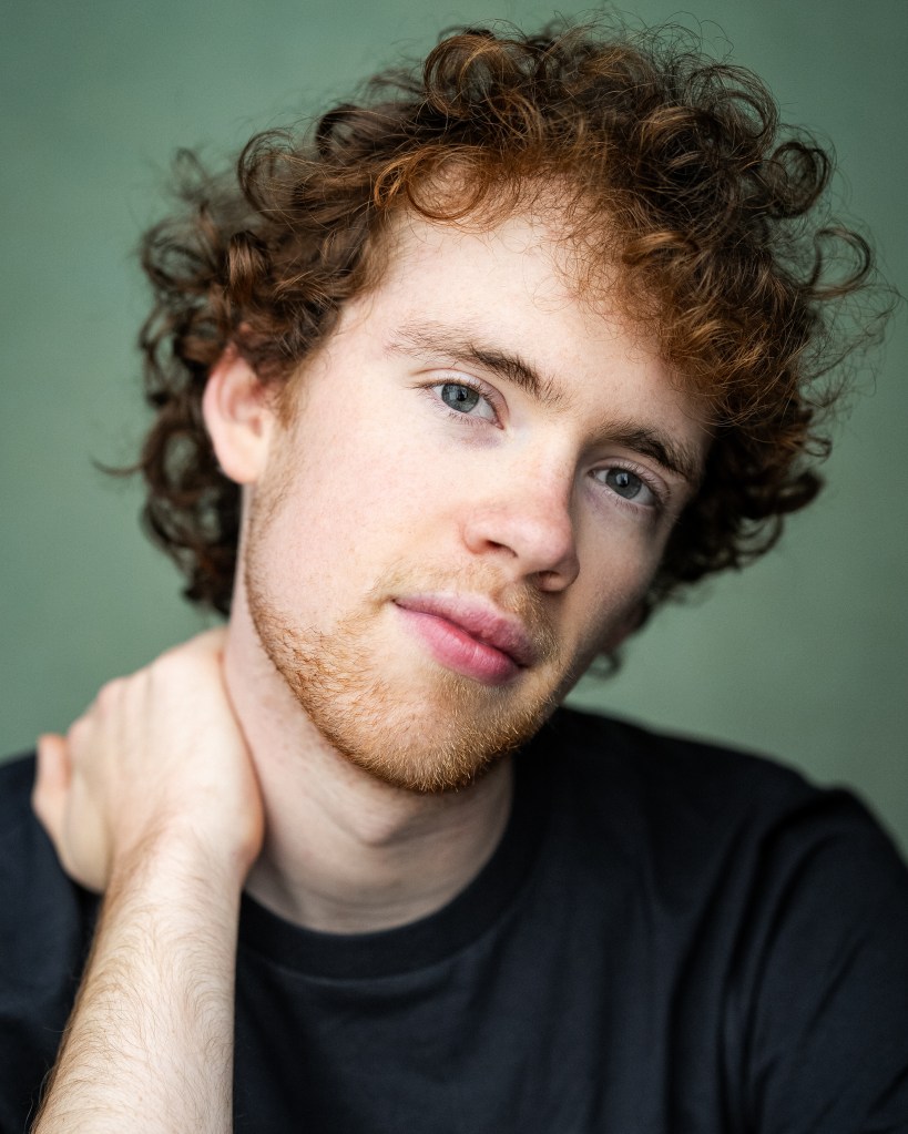A picture of Macsen, a white man in his early twenties with curly red hair and blue eyes.